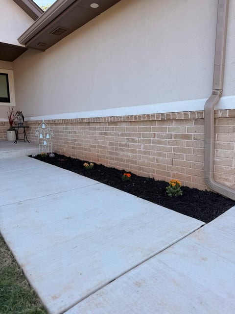 Modern garage with concrete floor, brick wall, small landscaped flower bed with black mulch and colorful plants along the base