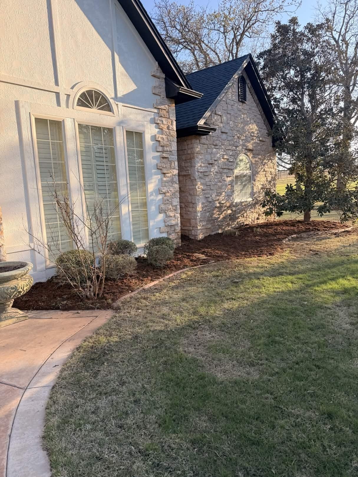 Modern two-story residential home with white and brick exterior, large windows, manicured lawn, and landscaped garden beds with bare trees