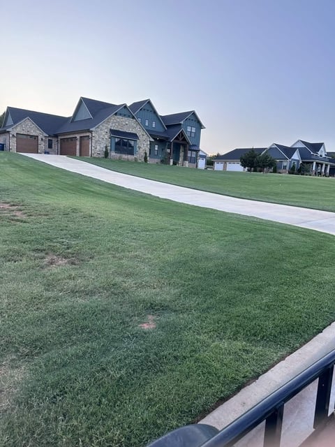 Large stone and brick residential home on expansive green lawn with white driveway in suburban neighborhood